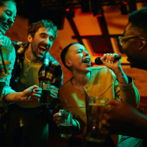 Happy African American woman signing karaoke and having fun with her friends in a bar at night.