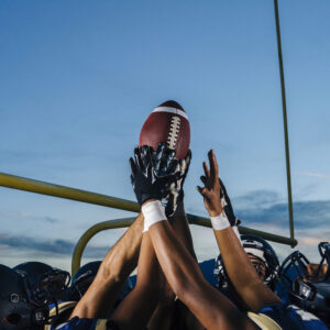 Victorious teenage and young male american football team holding up ball